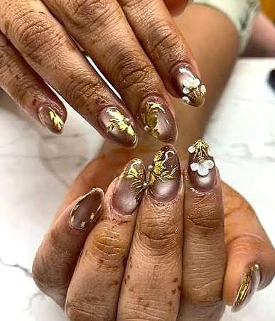 Mocha-brown almond nails with gold leaf, white 3D flowers and a butterfly
