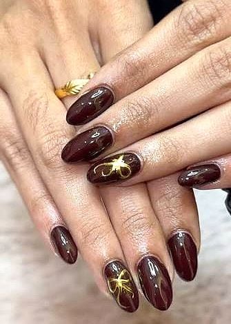 Glossy deep-burgundy almond nails with gold bow detailing
